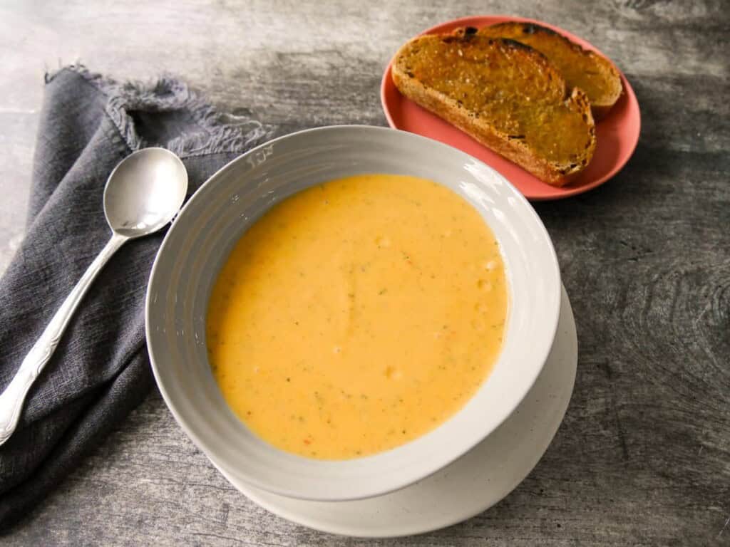 A bowl of courgette and pepper soup served with a side of toasted bread.