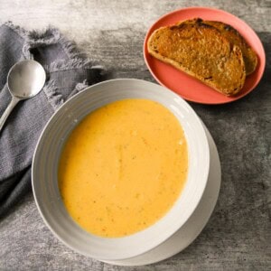 A bowl of courgette and pepper soup served with a side of toasted bread.