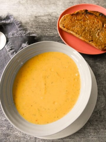 A bowl of courgette and pepper soup served with a side of toasted bread.