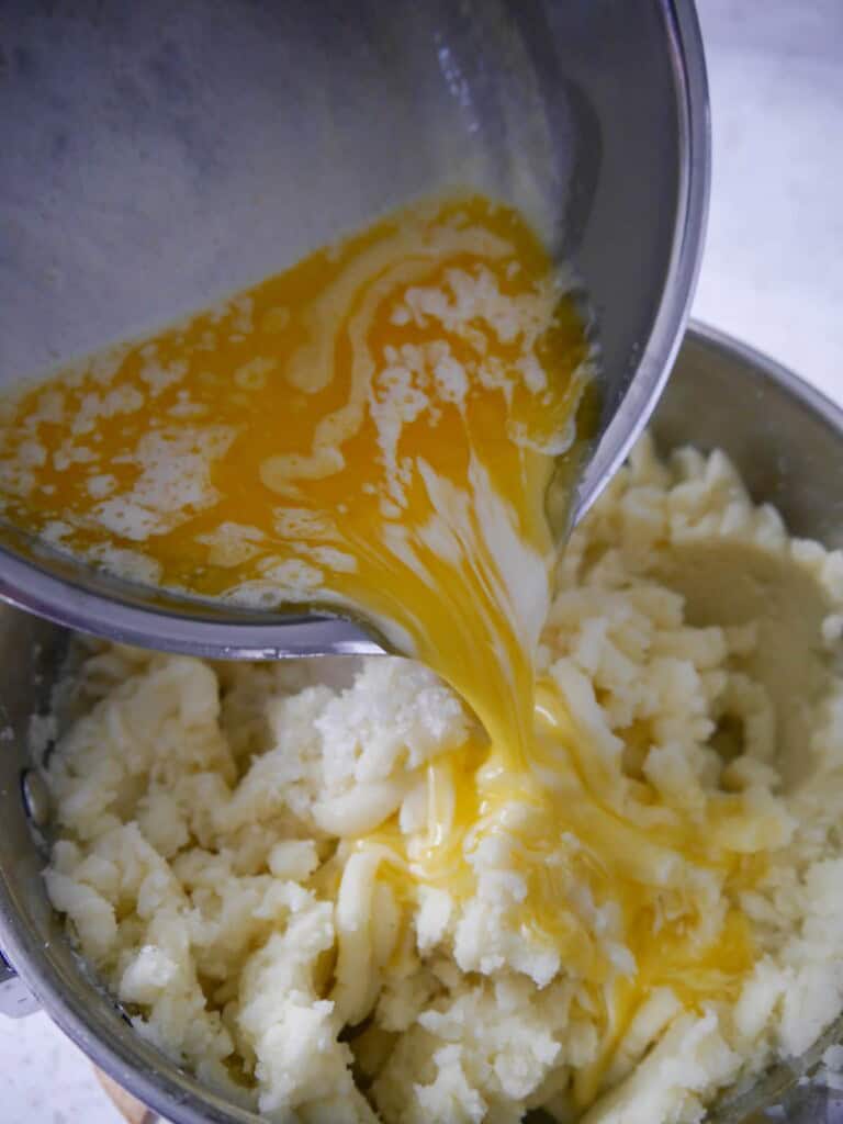A saucepan of mashed potatoes with melted butter and warm cream being added.