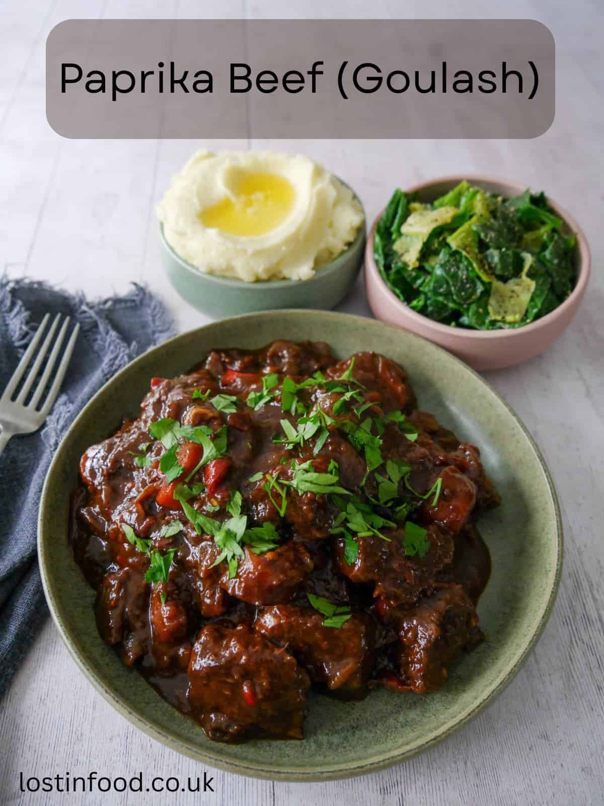Pinnable image with recipe title and a bowl of paprika beef garnished with chopped parsley, with bowls of creamy mashed potato and buttered spring greens set alongside.