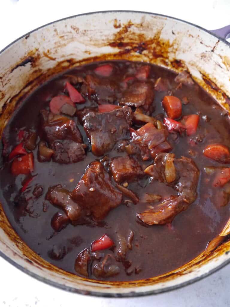 A Dutch oven filled with cooked paprika beef, with large chunks of beef, carrot and onion.