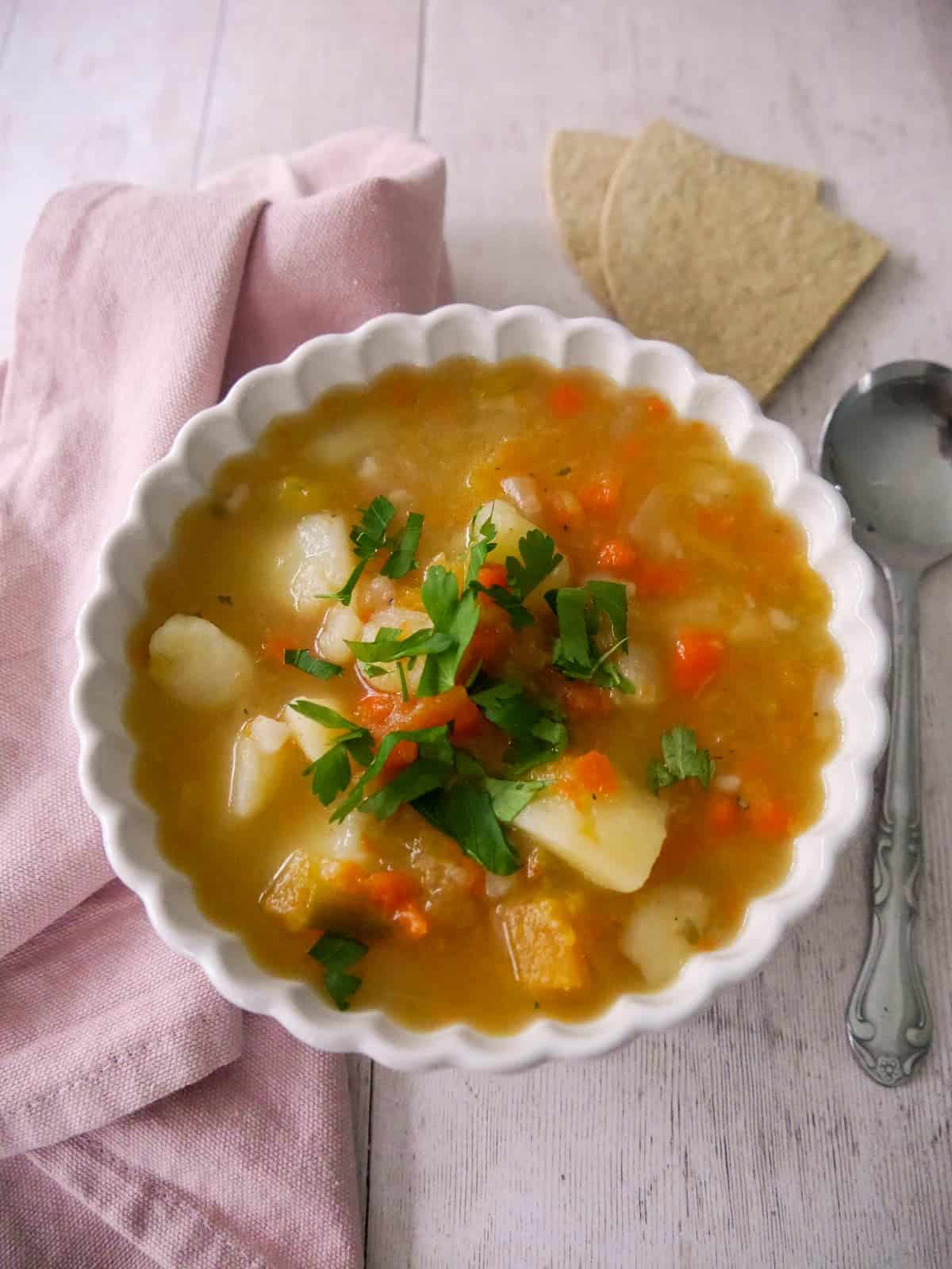A bowl of potato and vegetable soup with some oatcakes served alongside.