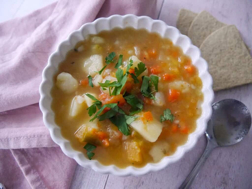 A bowl of potato and vegetable soup with some oatcakes served alongside.