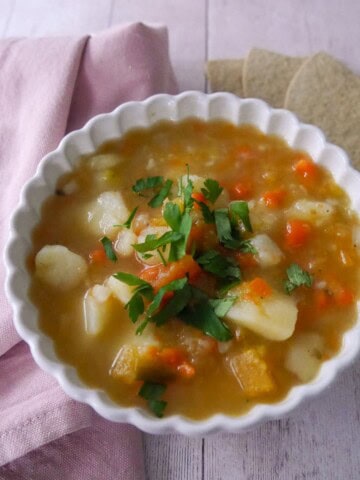 A bowl of potato and vegetable soup with some oatcakes served alongside.