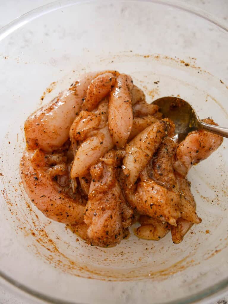 A small bowl of sliced raw chicken breast covered in a Cajun spice marinade.
