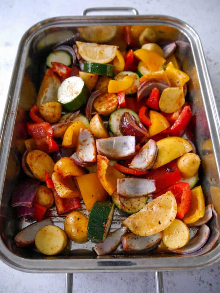 A baking tray filled with spiced and seasoned chunks of fresh vegetables and lemon wedges.