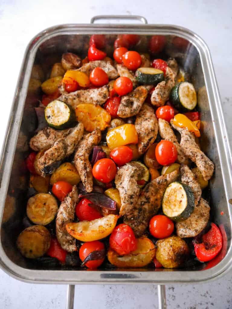 Baking tray with cooked Cajun chicken pieces on top of a bed of roasted vegetables.