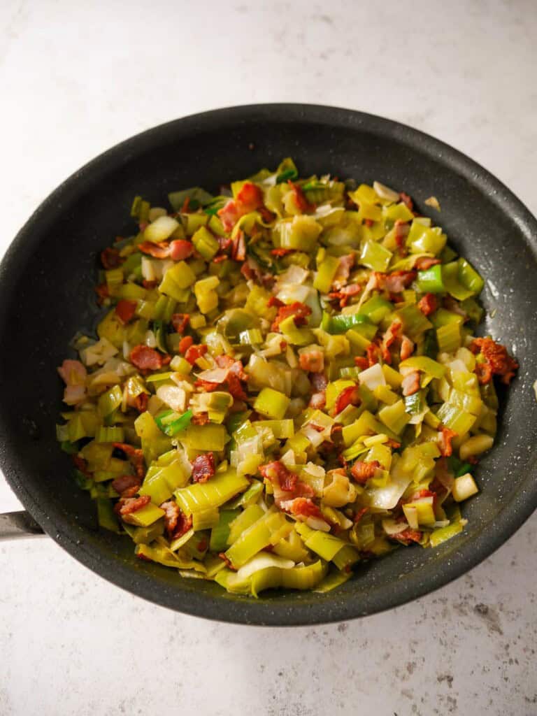 A large frying pan of sauteed bacon and leek.