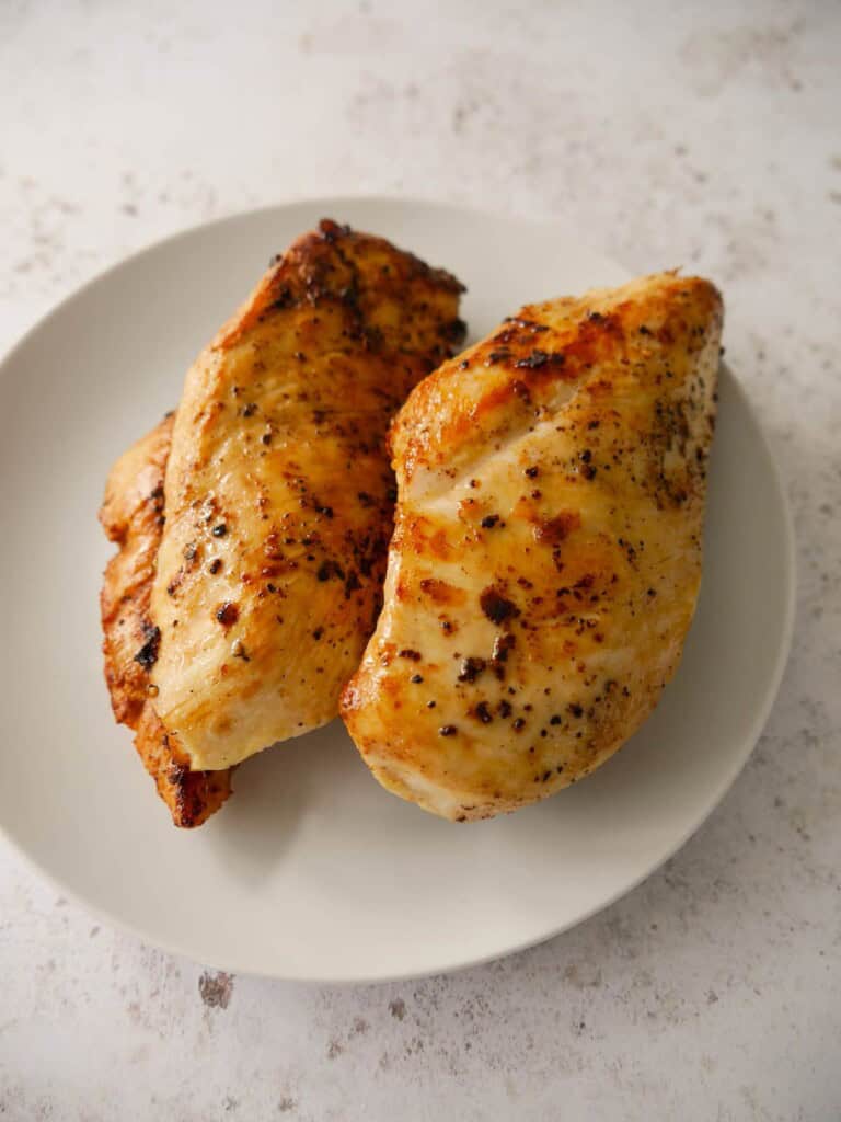 A plate with 2 large chicken breasts, seasoned with salt and black pepper and cooked until golden brown.