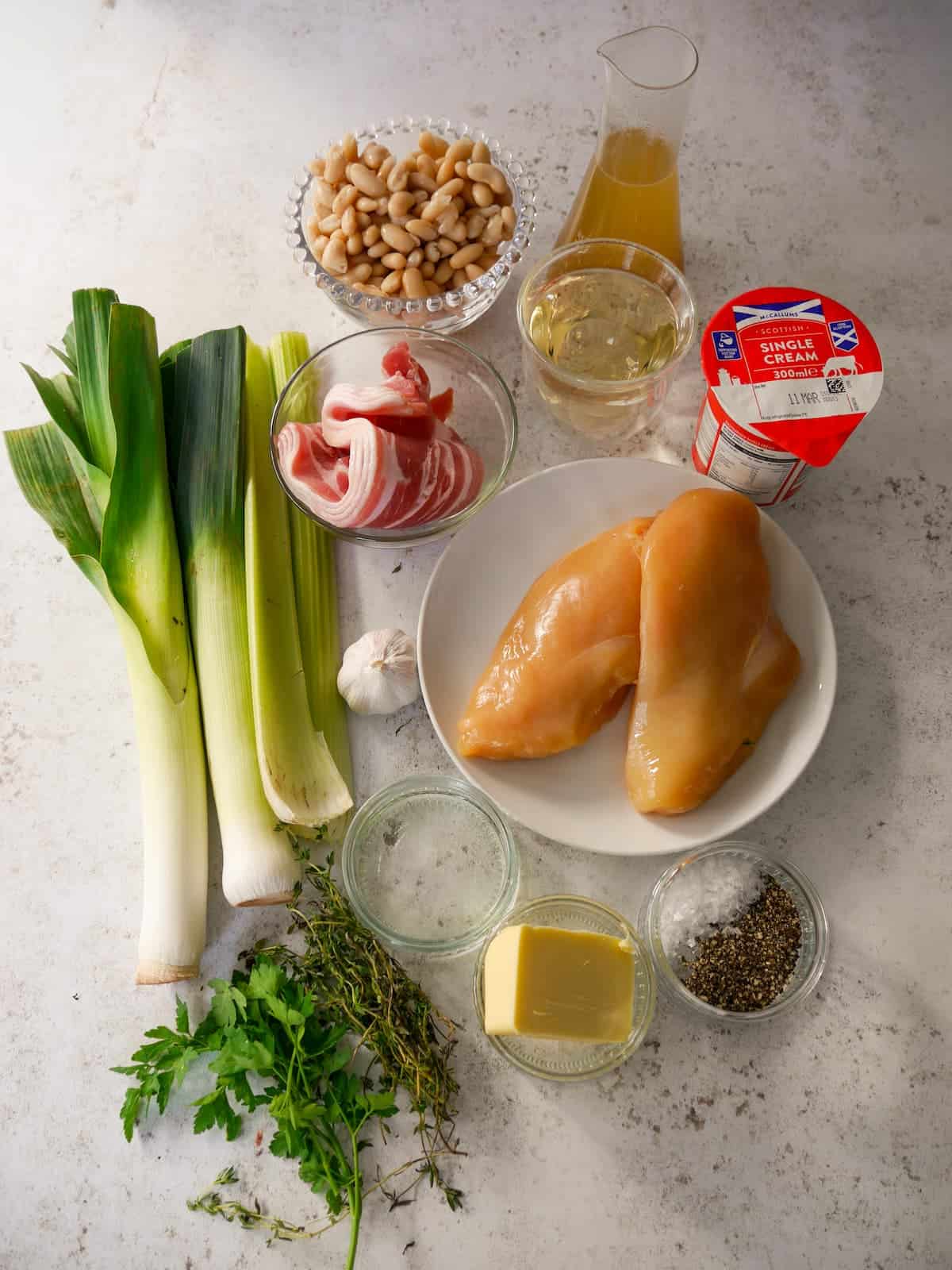 Individual recipe ingredients for making cannellini bean stew with bacon, leek and herbs, and served with pan fried chicken breasts.