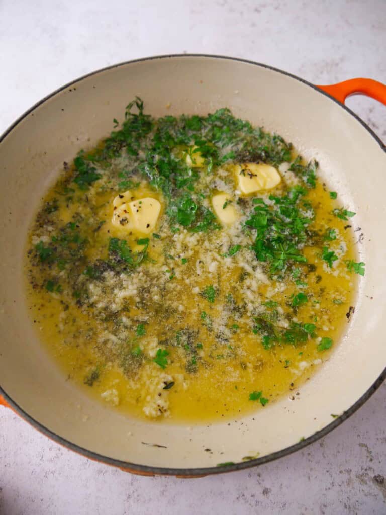 A large skillet of melted garlic and herb butter.