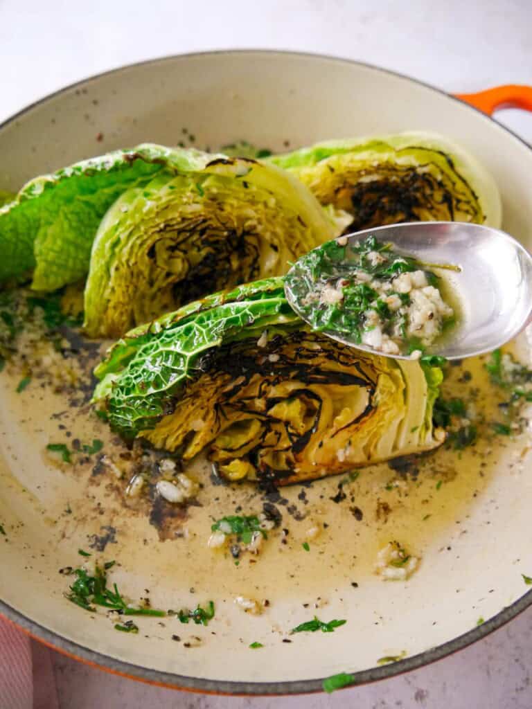 Melted garlic and herb butter being spooned over wedges of charred savoy cabbage.