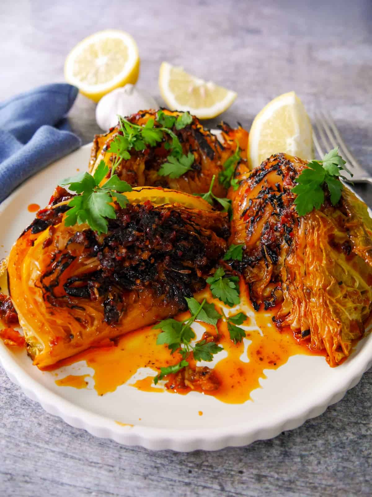 A plate of 3 charred wedges of savoy cabbage cooked in a harissa and lemon butter, garnished with fresh parsley and serve with a wedge of lemon.