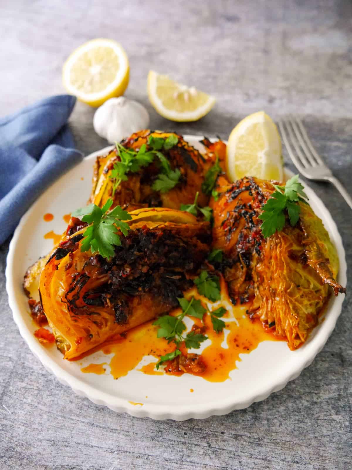 A plate of 3 charred wedges of savoy cabbage cooked in a harissa and lemon butter, garnished with fresh parsley and serve with a wedge of lemon.
