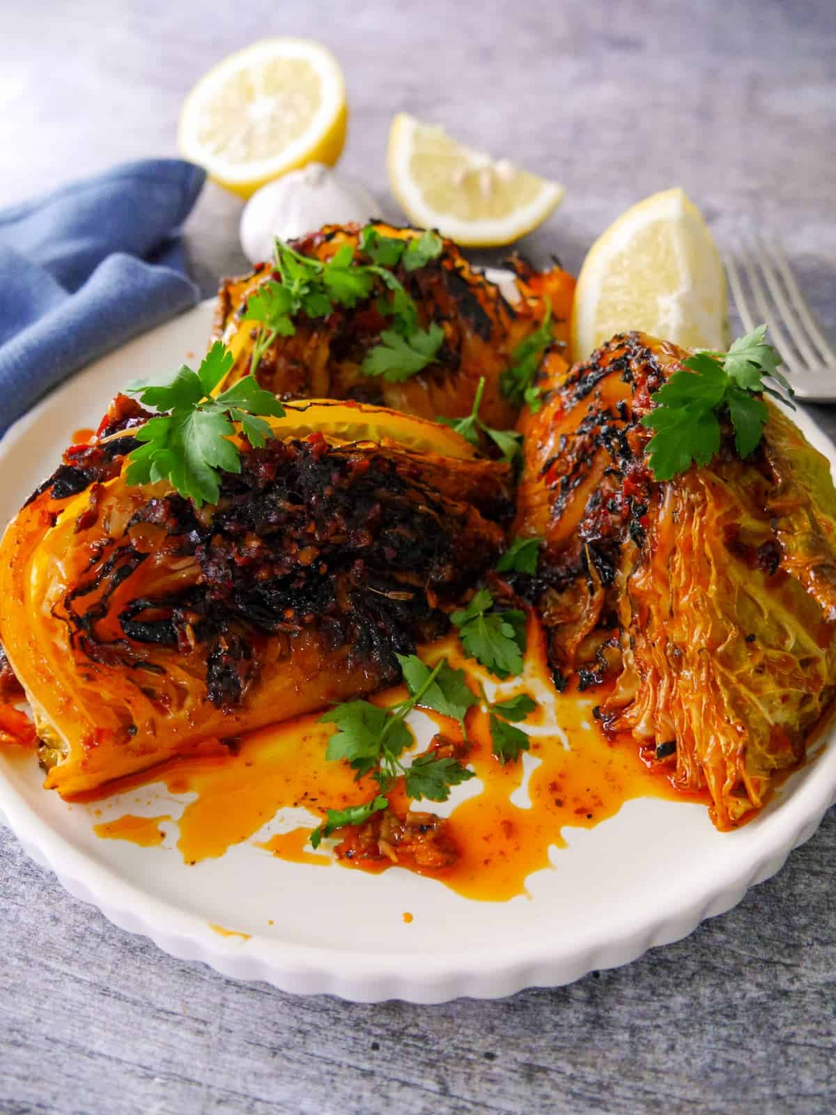 A plate of 3 charred wedges of savoy cabbage cooked in a harissa and lemon butter, garnished with fresh parsley and serve with a wedge of lemon.