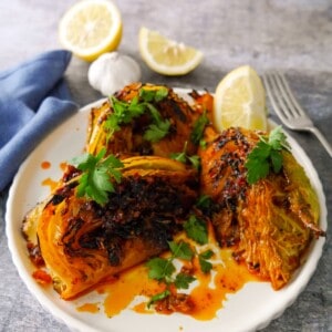 A plate of 3 charred wedges of savoy cabbage cooked in a harissa and lemon butter, garnished with fresh parsley and serve with a wedge of lemon.