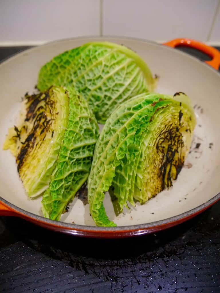 3 wedges of savoy cabbage being charred in a large skillet.
