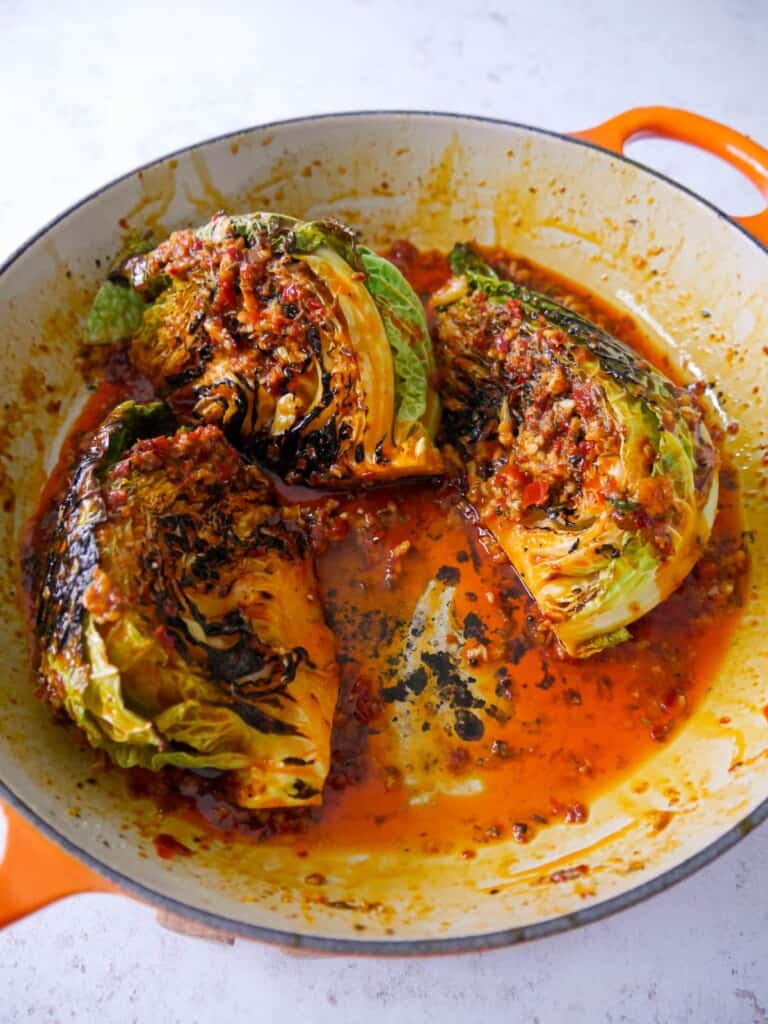 A large skillet with wedges of charred savoy cabbage, covered in a harissa and lemon butter.