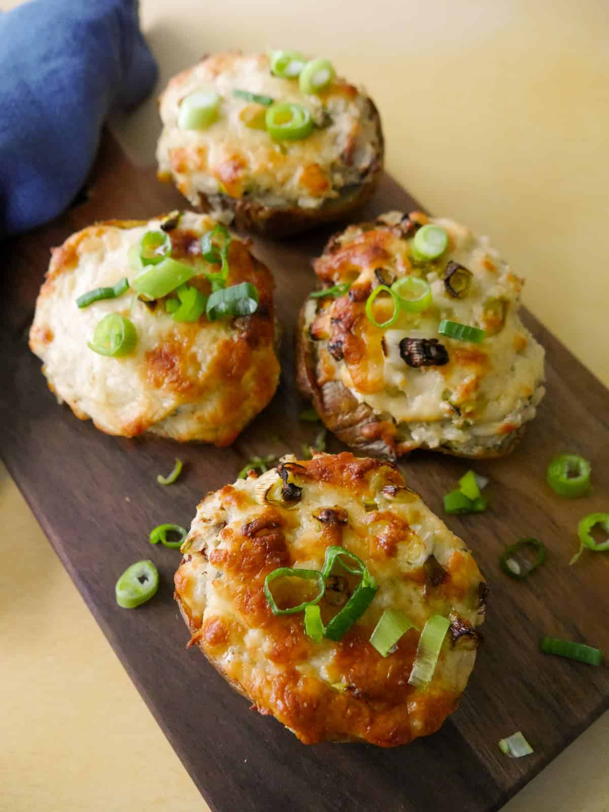 A wooden board topped with cheesy potato skins with a melted cheese and spring onion topping.
