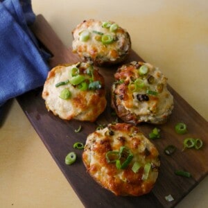 A wooden board topped with cheesy potato skins with a melted cheese and spring onion topping.