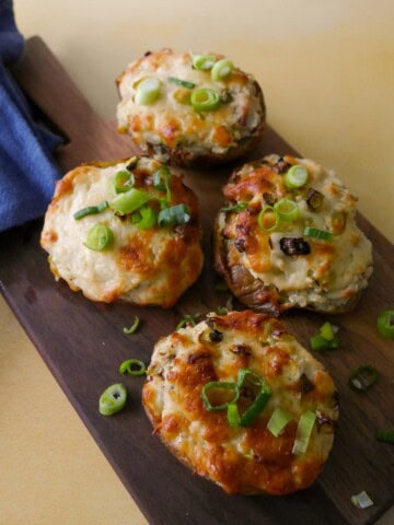 A wooden board topped with cheesy potato skins with a melted cheese and spring onion topping.