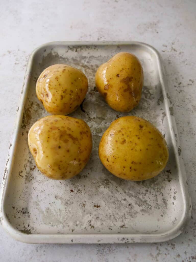 Four large potatoes covered with a little olive oil and set on a baking tray.