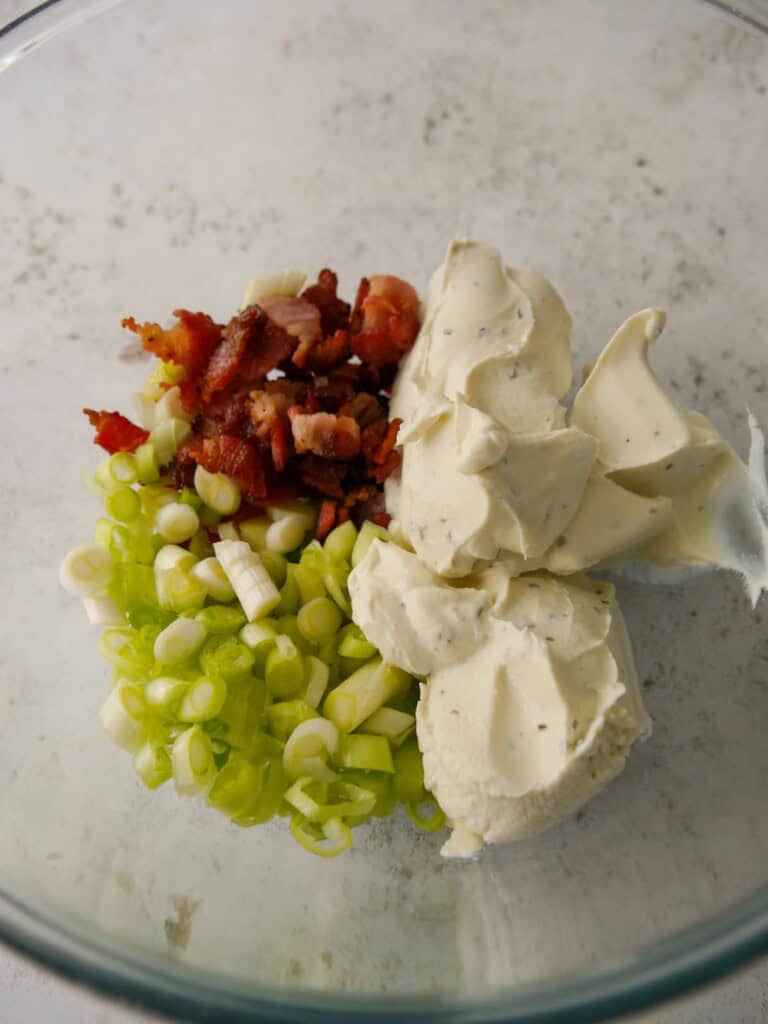 A bowl of crispy bacon pieces, sliced spring onion and garlic and herb cream cheese.
