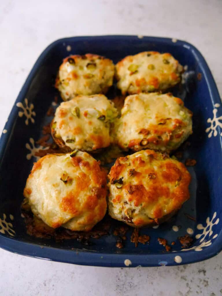 An oven proof dish with cooked cheesy potato skins with added bacon and spring onions and topped with melted cheese.