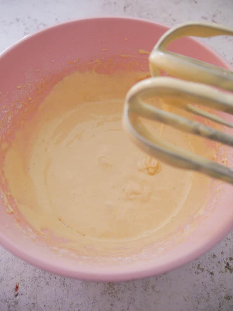 A bowl of whisked eggs and sugar with added flour.