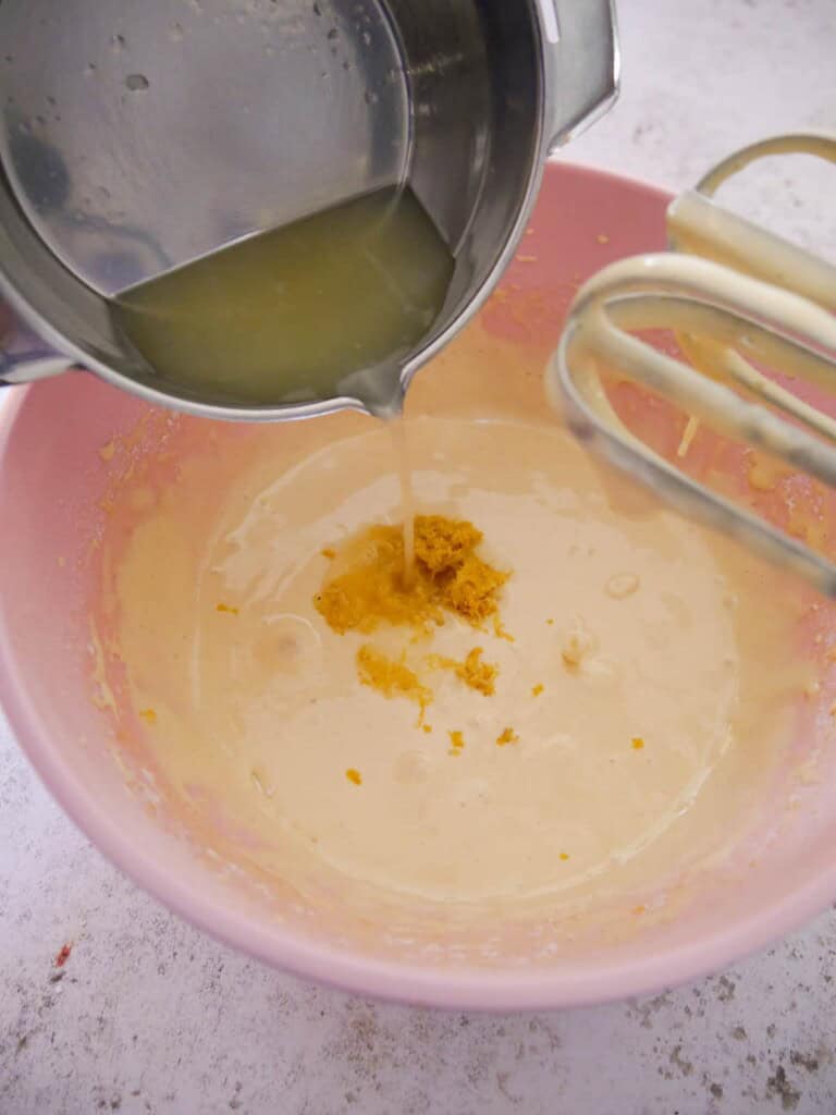 A bowl of madeleine cake batter with lemon zest and juice being added.