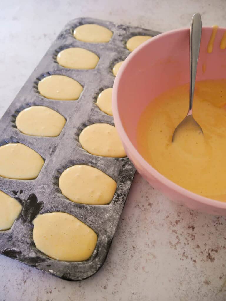 A madeleine baking tray filled with cake batter, with a bowl of the batter set alongside.