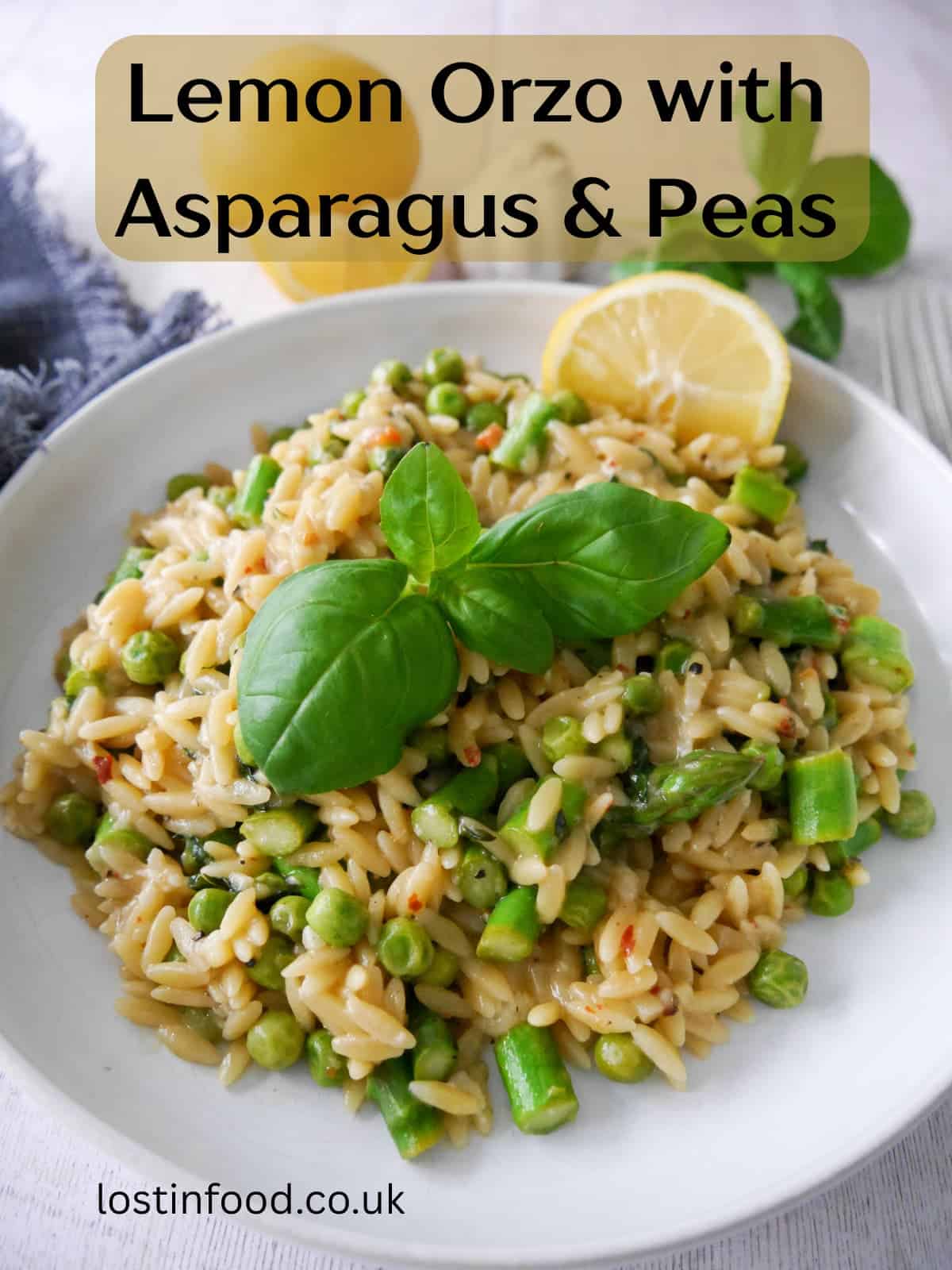 Pinnable image with recipe title and a white bowl of lemon orzo with asparagus and garden peas, garnished with fresh basil and served with a wedge of lemon.