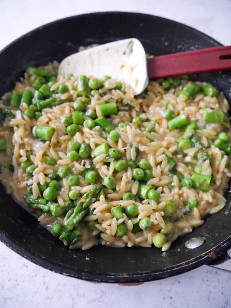 A non stick frying pan filled with lemon orzo pasta with asparagus and peas.