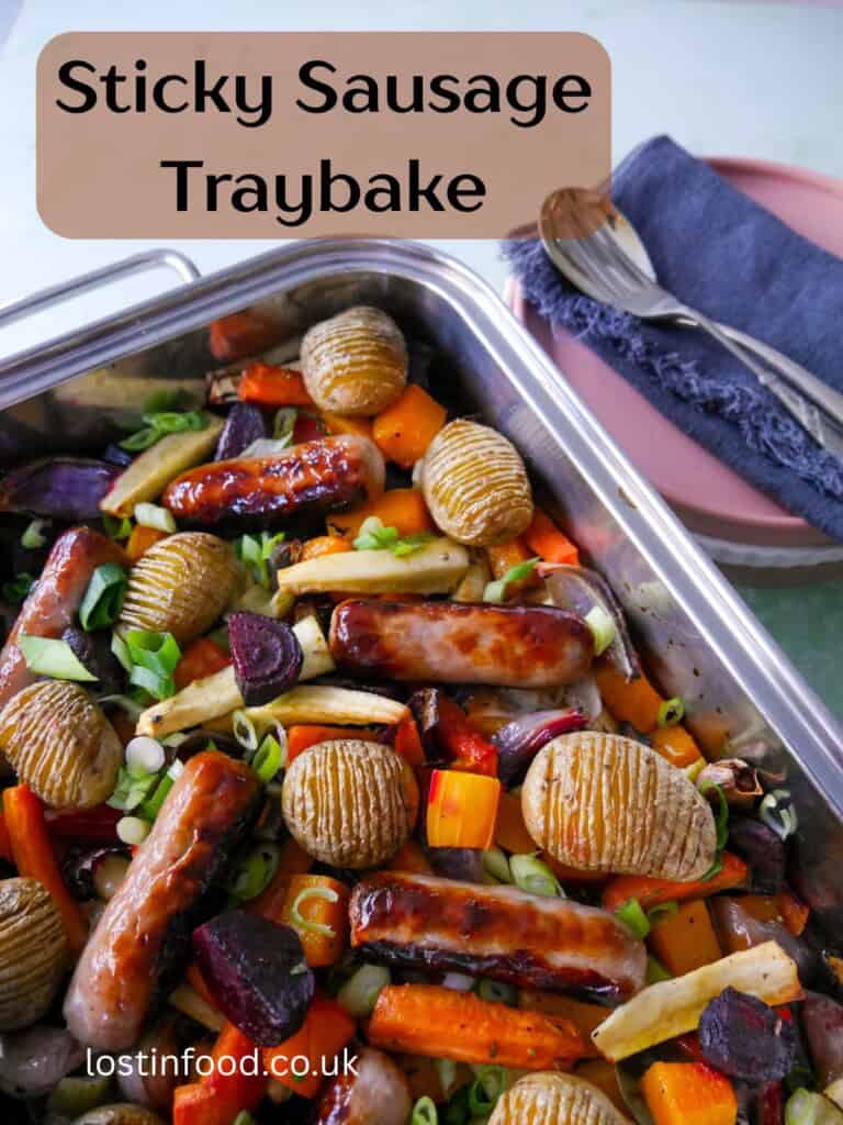 Pinnable image with recipe title and a large high sided baking tray filled with roasted root vegetables, hasselback potatoes and pork sausages.