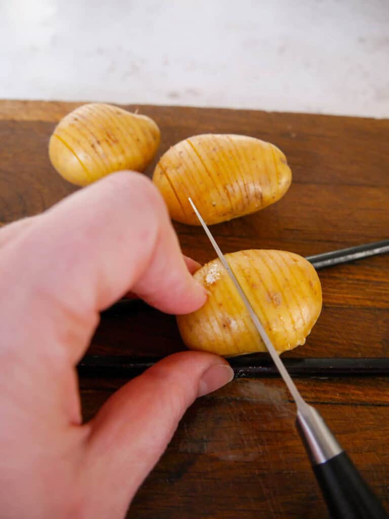 A baby potato resting between 2 chopsticks, being sliced into ¾ way down to form slits along the potato.