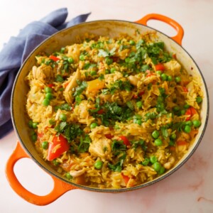 A large skillet of curried chicken and rice with added vegetables and cashew nuts, and garnished with coriander leaf.