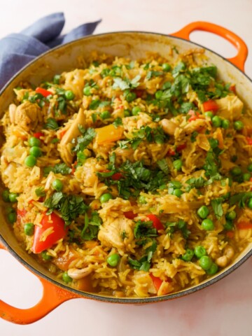 A large skillet of curried chicken and rice with added vegetables and cashew nuts, and garnished with coriander leaf.