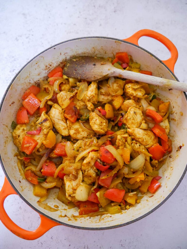 A large skillet of sauteed chicken and vegetables with dry spices.