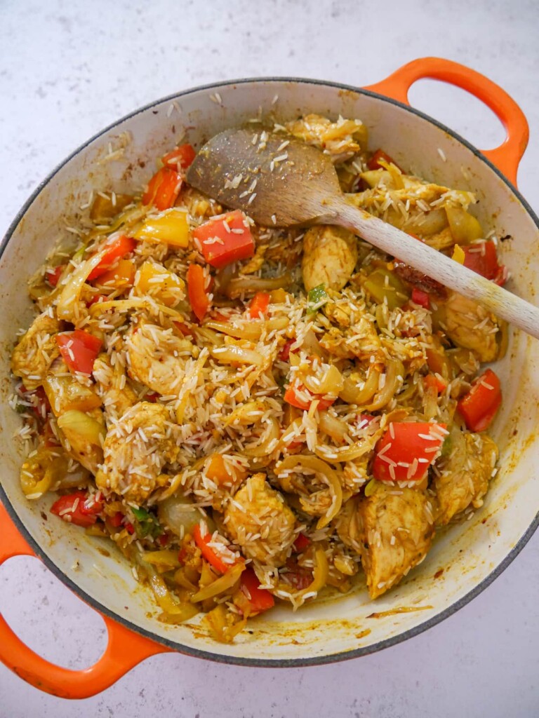 A large skillet with sauteed chicken and vegetables with added white rice.