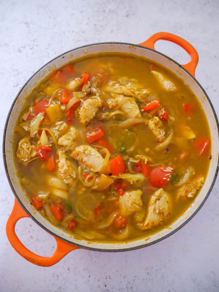 A large skillet of A large skillet with sauteed curried chicken and vegetables, with added white rice and chicken stock.