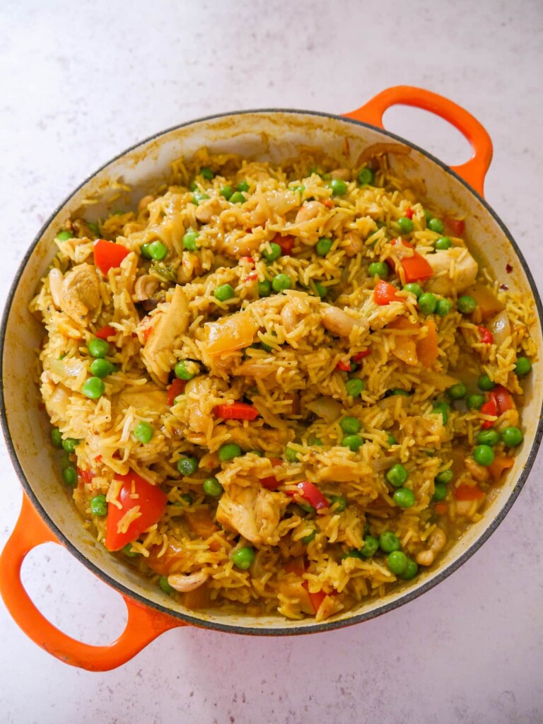 A large skillet with sauteed curried chicken and vegetables, cooked with rice and with added garden peas and cashew nuts.