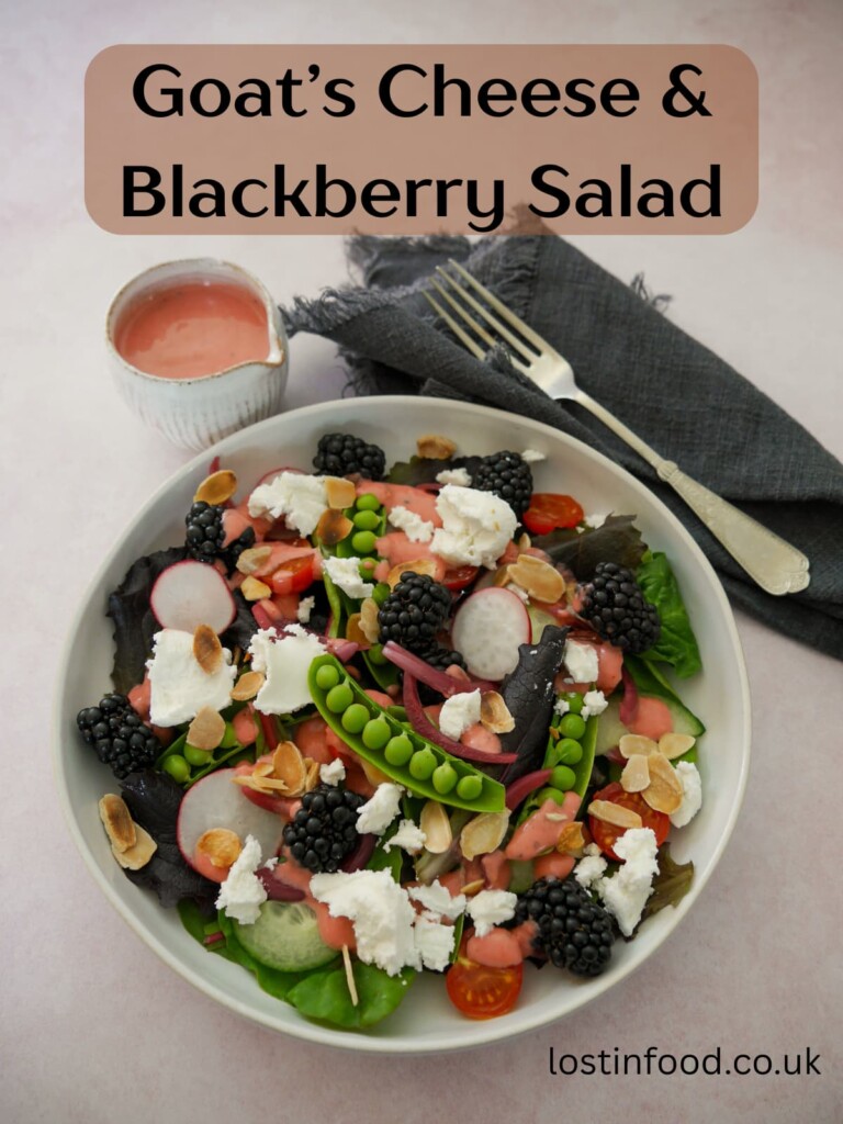 Pinnable image with recipe title and a bowl of mixed salad leaves, radish, tomato, cucumber, sugar snap peas, pickled red onions, with goat's cheese and blackberries served with a small jug of raspberry vinaigrette.