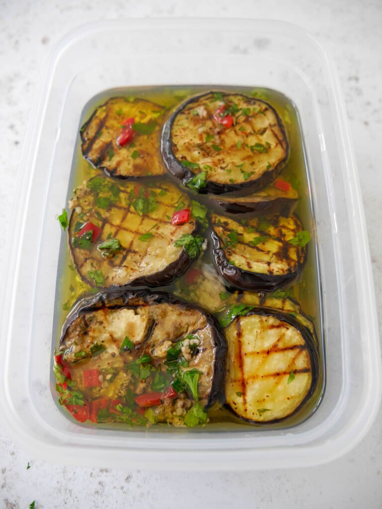 A large plastic storage dish filled with Italian marinated aubergine covered in olive oil.