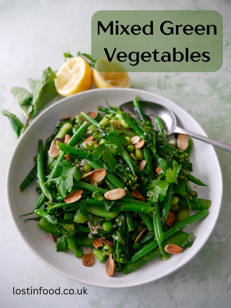 Pinnable image with recipe title and a bowl of mixed green vegetables including tenderstem broccoli, green beans, sugar snap peas, garden peas and edamame beans, coated with a garlic and herb butter with added toasted flaked almonds.