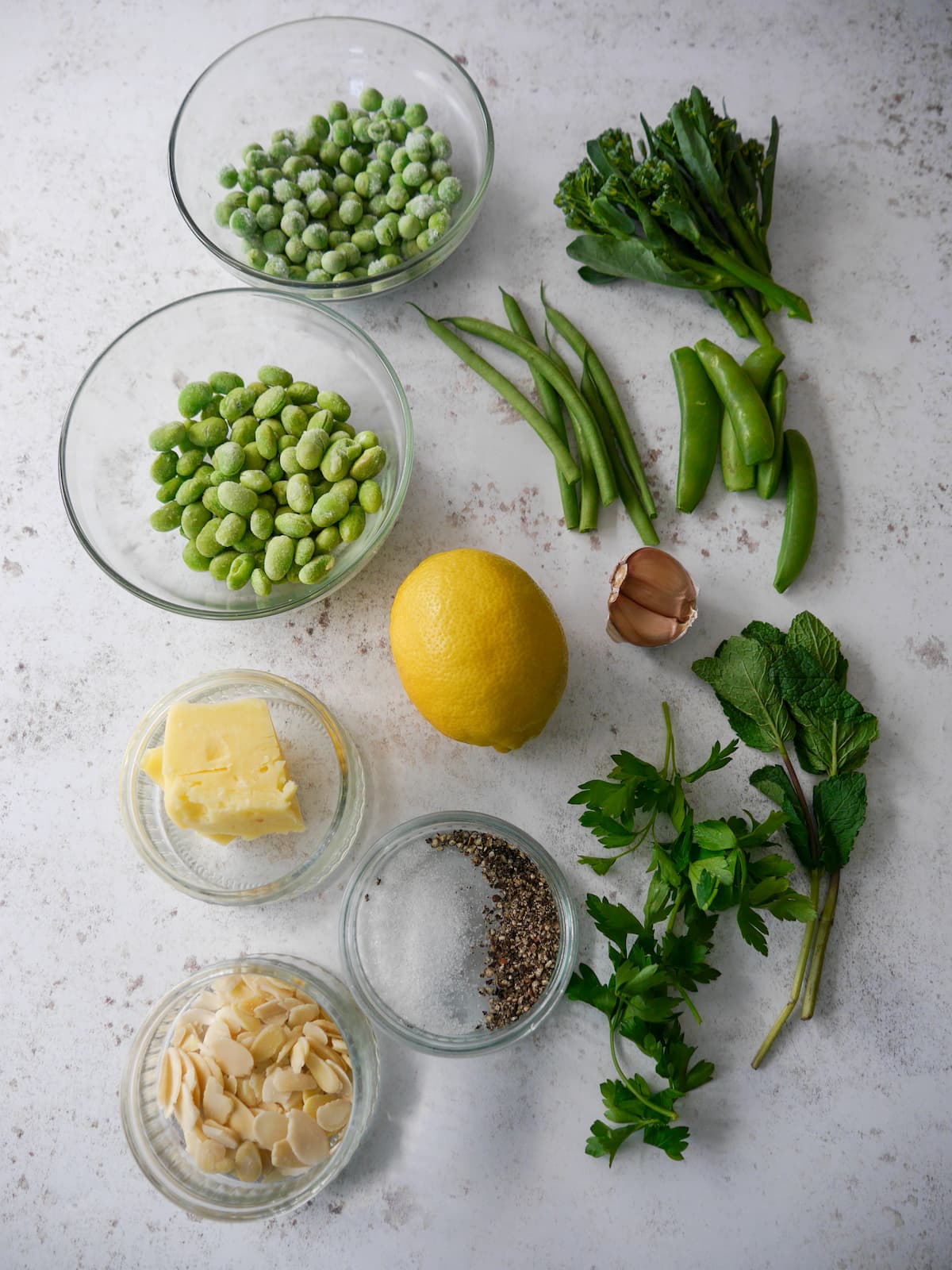 Individual recipe ingredients for making mixed green vegetables with a herb and lemon butter.