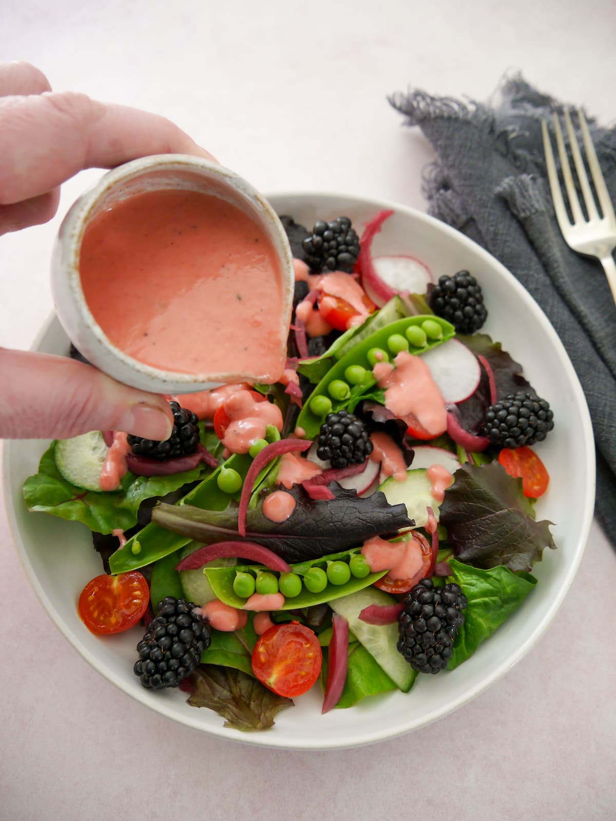 A bowl of mixed salad leaves and vegetables with a small jug of fresh raspberry vinaigrette dressing being poured over.