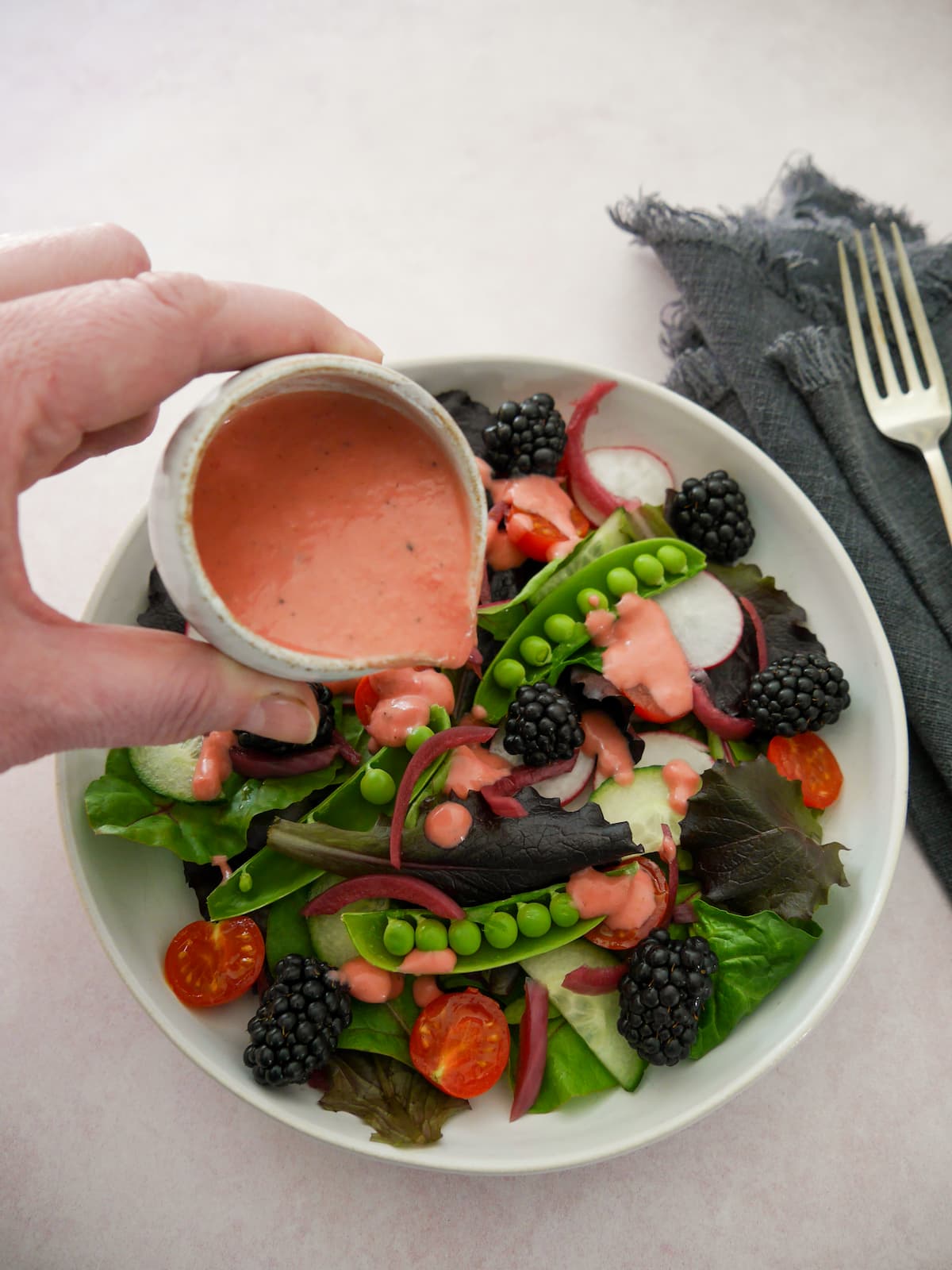 A bowl of mixed salad leaves and vegetables with a small jug of fresh raspberry vinaigrette dressing being poured over.