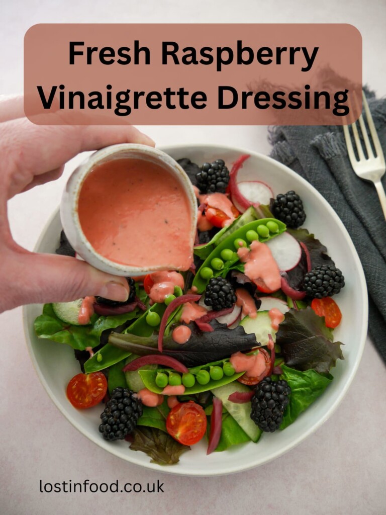 Pinnable image with recipe title and a bowl of mixed salad leaves and vegetables with a small jug of fresh raspberry vinaigrette dressing being poured over.