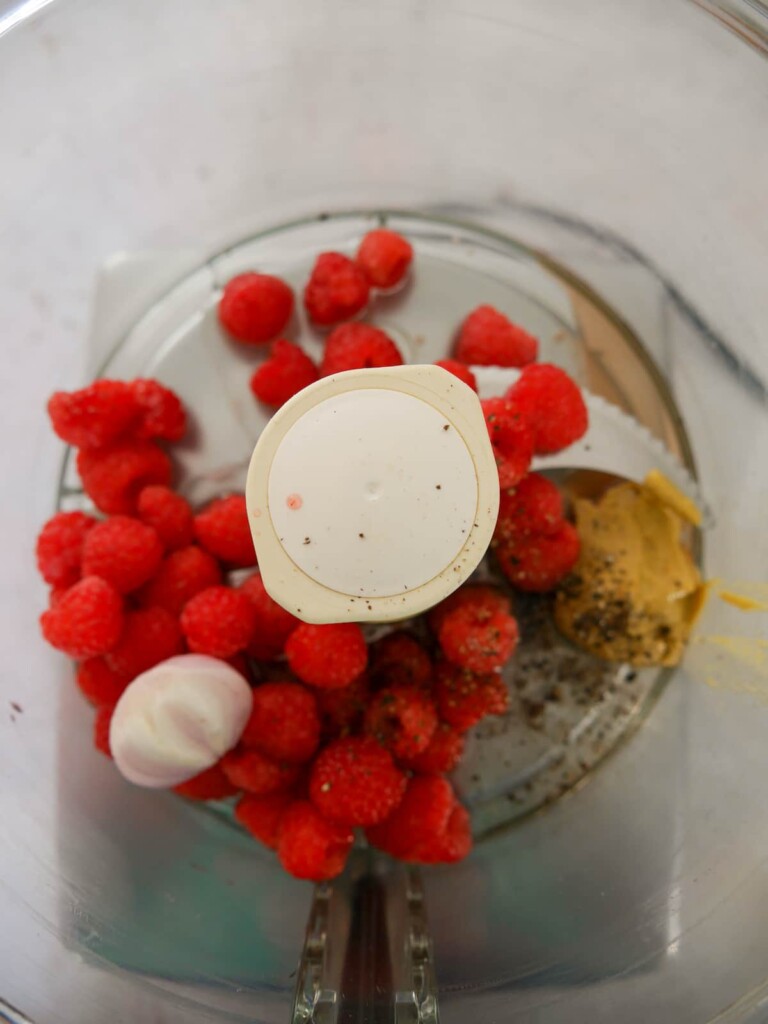 A food processor bowl filled with the ingredients for making fresh raspberry vinaigrette.